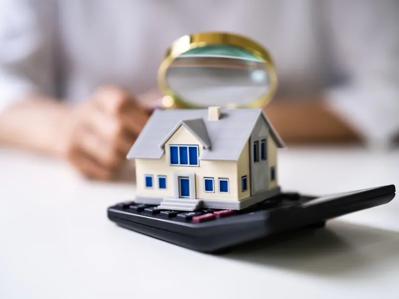 Model house on a calculator with a magnifying glass, representing a pre-purchase roof condition check